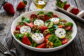 Fresh salad - goat cheese, strawberries, walnuts, cherry tomatoes and leafy greens on wooden table
