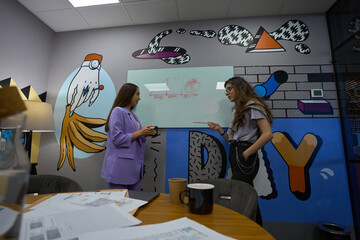 Two women stand at whiteboard and look at each other