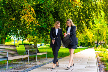 Two beautiful women walking in city park looking at watch