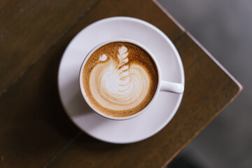 A cup of cafe latter with latte art in white cup with wooden table background