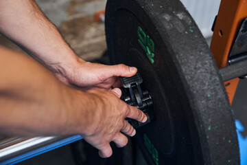 Sportsman adjusting weight plates at the barbell while preparing for the hard training