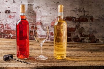 Bottles of rosé and white wine next to a glass and a corkscrew, on an aged wooden table, close-up.