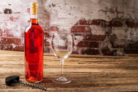 Bottle of rose wine next to a glass and a corkscrew, on an aged wooden table, close-up.