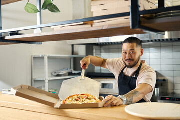 Contented cook packing up fresh pizza for takeaway