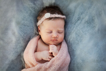 Sleeping newborn baby girl swaddled in knitted pink plaid on soft blue background