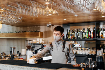 A masked barista exquisitely serves ready-made coffee in a modern cafe during a pandemic. Serving ready-made coffee to a client in a cafe.