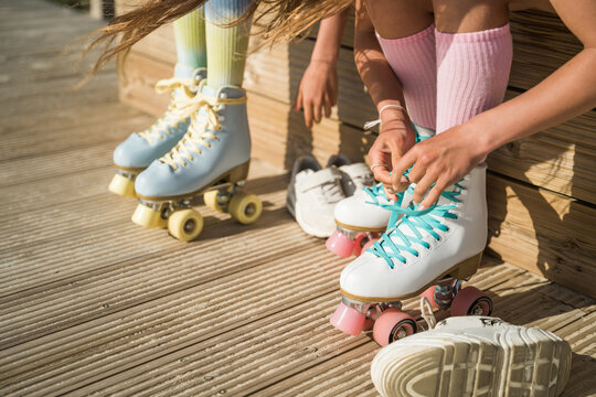 Two child girls in high socks tying laces at their roller skates while preparing for the riding