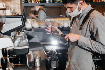 A masked barista prepares an exquisite delicious coffee at the bar in a coffee shop. The work of restaurants and cafes during the pandemic.