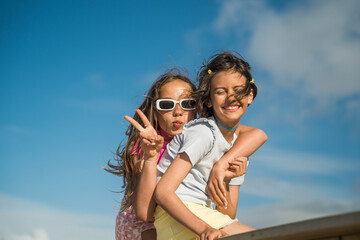 Smiling kid girls gesturing and embracing while having fun on the bridge