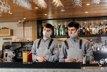 Two stylish bartenders in masks and uniforms are preparing cocktails at a party during a pandemic. The work of restaurants and cafes during the pandemic.
