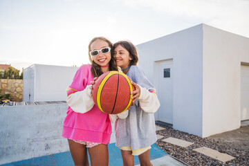 Cheerful girls holding game ball and posing to the camera after basketball playing