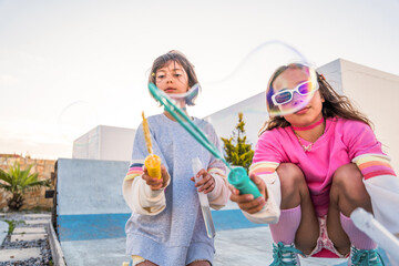 Positive children wearing bright clothes blowing soap bubbles at the open air stadium