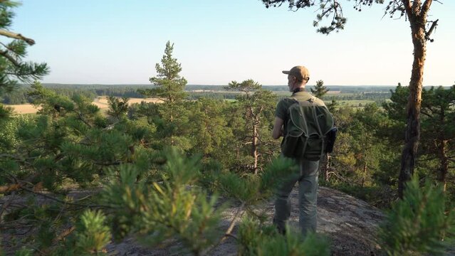 Mature man with hiking equipment walking in mountain forest in Finland and photographing breathtaking northern landscapes with an old vintage camera