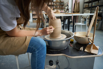 Fototapeta na wymiar Woman making clay vase on potter wheel