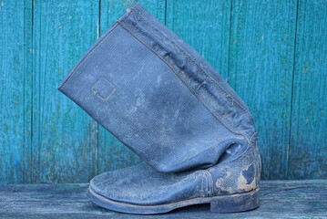 one old black dirty tarpaulin boot stands on a gray table against a green wall