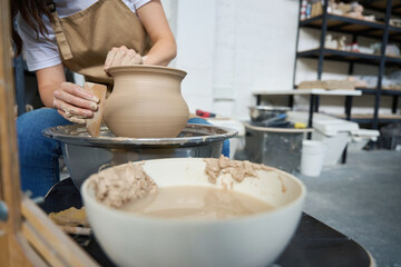 Woman potter working on a potter's wheel with clay vase