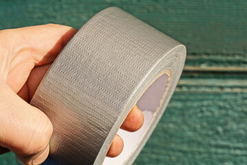 a hand holds one skein of gray reinforced tape on a green background