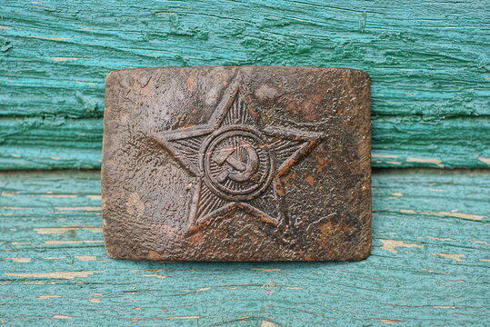 one old brown metal large Soviet belt buckle with a star lies on a green wooden table