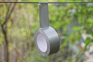 one gray round roll of reinforced tape hanging on a wire on the street on a green background