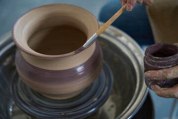 Close-up of clay pot and hands of craftsman with brush