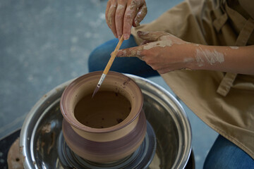 Potter decorates an earthenware jug with brush on potter wheel