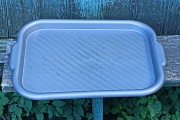 one large gray empty plastic tray stands on a wooden table against a green wall in the vegetation...