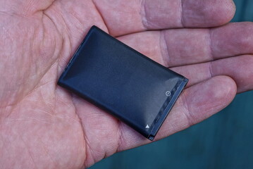 one black rechargeable battery from a mobile phone lies in the palm of your hand on a green...