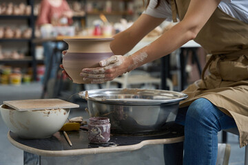 Master sits potter wheel and holds clay product in his hands