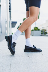 Female legs in leather shoes, white socks with and black moccasins, black shorts, fashion details