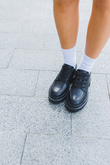 Female legs in leather shoes, white socks with and black moccasins, black shorts, fashion details