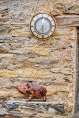 Handcrafted wooden sculpture, representing a stylized boar, and a vintage clock hanged on a stone wall.