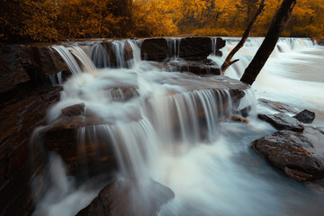 Water cascade flows over a rock stack in an Arkansas creating a scenic waterfall during autumn. 