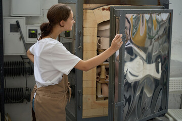 Woman stands in front of open door of pottery kiln