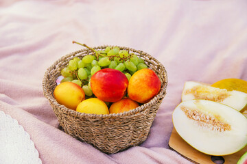 A fruit basket, grapes, peaches, watermelon, melon lie on a blanket. Straw hat and glasses. Picnic in nature.