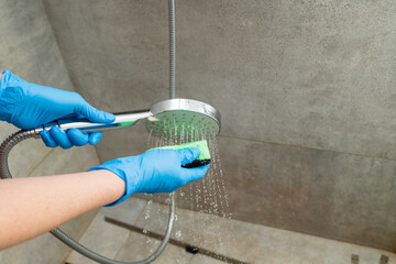 A woman cleans a shower head from limestone.