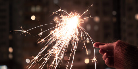 Hand holding sparkler. Sparkler with blurred busy city light background. Festive sparklers at night.