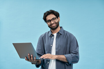 Happy young arab business man student or employee standing isolated on blue background holding laptop advertising web products for elearning, education training and webinars, working online.