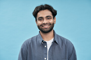 Smiling confident young adult arab man standing isolated on blue background. Happy ethnic guy student or professional employee wearing shirt looking at camera posing for headshot portrait.