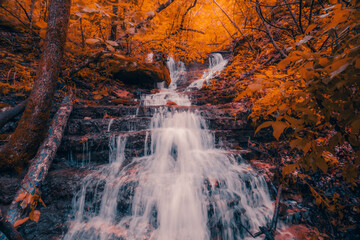 Cascading waterfall flows down an Arkansas mountain with orange fall colored autumn leaves at Lost Valley