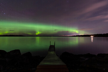 Northern lights, wooden pier and reflections in the water. Nykarleby/Uusikaarlepyy, Finland