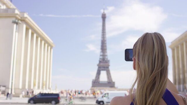 Young woman using her phone to take a picture of the Eiffel Tower in Paris, France