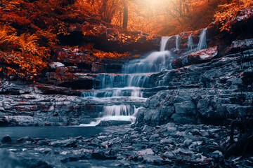 Copperhead falls waterfall under magical light in the peak of autumn deep in the Ozark mountains of Arkansas with red fall leaves and cold rigid rocks..  