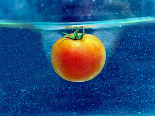 red tomato in water with bubbles on a dark background.