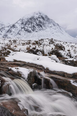 Fototapeta na wymiar Majestic Winter landscape image of River Etive in foreground with iconic snowcapped Stob Dearg Buachaille Etive Mor mountain in the background