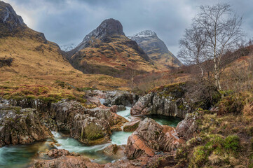 Gorgeous landscape image of vibrant River Coe flowing beneath snowcapped mountains in Scottish Highlands - obrazy, fototapety, plakaty
