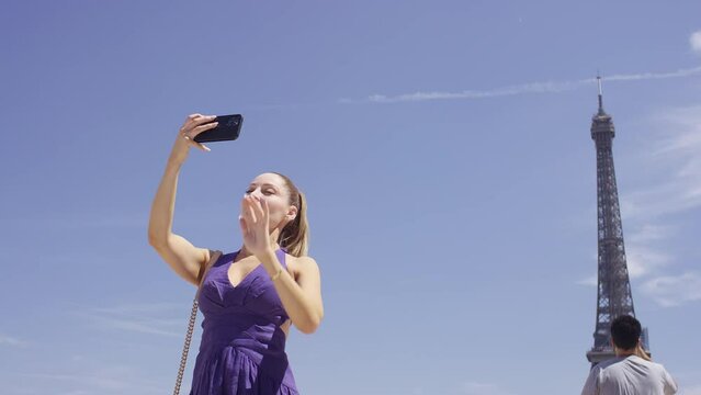 Beautiful young female in a purple summer dress takes a selfie photo with the Eiffel Tower behind her, in slow motion 