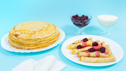 A large stack of thin pancakes on a white plate. Nearby is a plate with pancakes folded in triangles decorated with berries