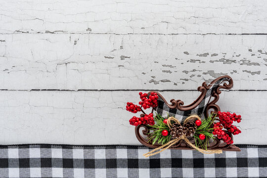 winter holiday theme with black and white gingham ribbon and a sled with pine cone and red berries on peeling wood background