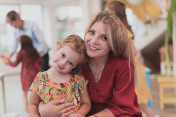 A cute little girl kisses and hugs her mother in preschool