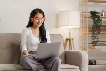 Fototapeta premium Smiling young asian woman enjoying free time while relaxing with her laptop in living room..